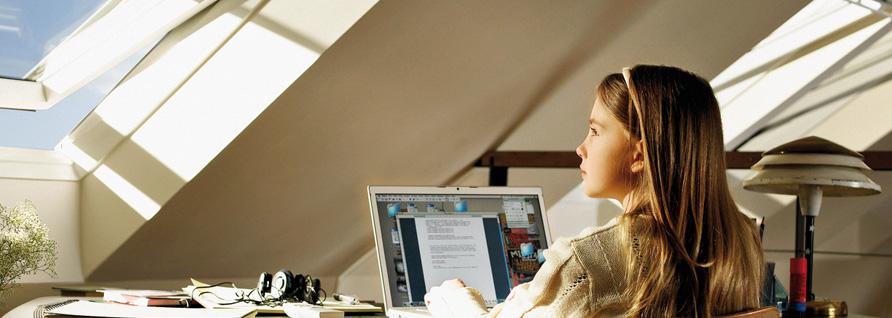 Ein Mädchen am Velux Dachfenster am Laptop